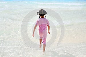 Little Asian child girl enjoys and running into big Swimming pool outdoor on holidays. Rear view children having fun