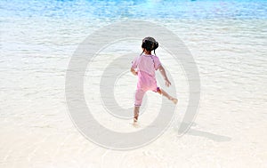 Little Asian child girl having fun and running into aqua park on holidays. Back view kid enjoys in big swimming pool outdoor