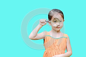 Little asian child girl looking through magnifiying glass isolated on cyan background