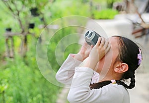 Little Asian child girl looking up in sky through the binoculars in the nature field outdoor. Explore and adventure concept