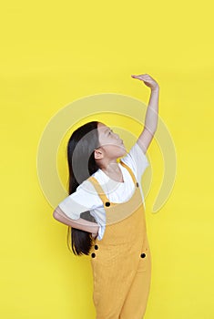 Little asian child girl measures the growth on yellow background. Kid estimate her height by hand