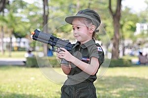 Little Asian child girl in pilot soldier suit costume with holding gun in hands at the garden