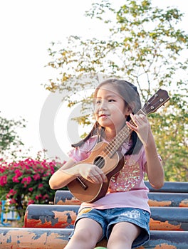 Little asian child girl play the ukulele, in the garden on the Steel pipe