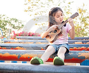 Little asian child girl play the ukulele, in the garden on the Steel pipe