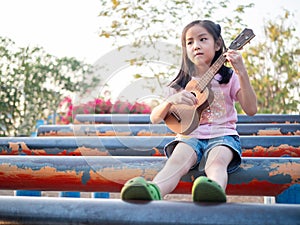 Little asian child girl play the ukulele, in the garden on the Steel pipe