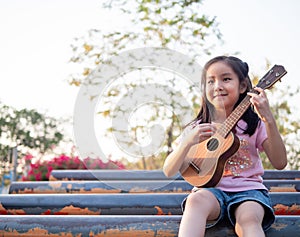 Little asian child girl play the ukulele, in the garden on the Steel pipe