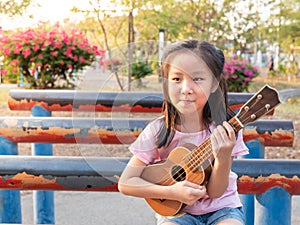 Little asian child girl play the ukulele, in the garden on the Steel pipe