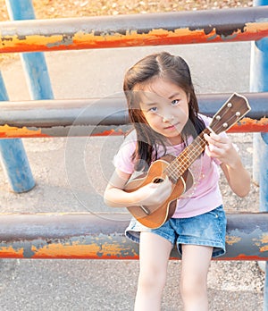 Little asian child girl play the ukulele, in the garden on the Steel pipe, practice to play