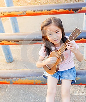 Little asian child girl play the ukulele, in the garden on the Steel pipe, practice to play