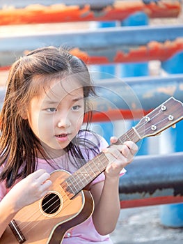 Little asian child girl play the ukulele, in the garden on the Steel pipe, practice to play