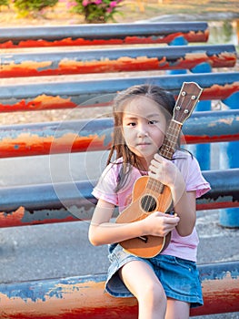 Little asian child girl play the ukulele, in the garden on the Steel pipe, practice to play