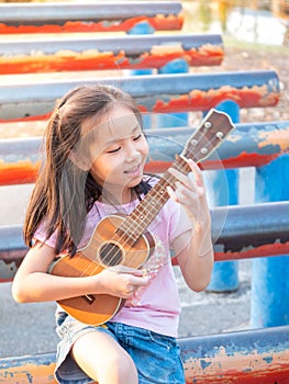 Little asian child girl play the ukulele, in the garden on the Steel pipe, practice to play