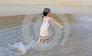 Little asian child girl running on the sea beach. Back view