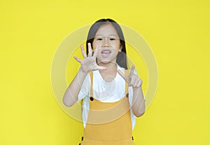 Little asian child girl showing finger number seven isolated on yellow background. Kid counting with fingers for education concept