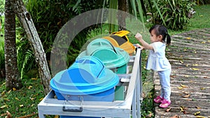 Little Asian child girl throwing empty plastic bottle into the recycle trash in park