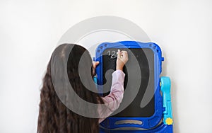 Little Asian child girl writing on blank black board over white background. Education concept. Rear view