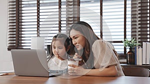 Little asian daughter online education using laptop computer with mother feeding noodles