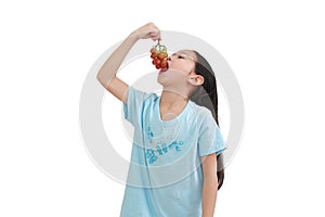 Little asian girl eating purple grape on white background. Kid holding bunch of grapes in the mouth