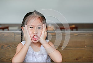 Little Asian girl with expression funny face lying on the wood table with looking at camera