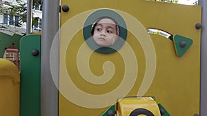 Little Asian girl face looks out the window of toy house at playground and looking sad. isolation child plays outdoors. children