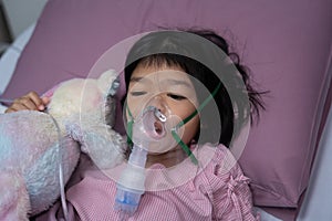 A little Asian girl has an oxygen mask and breathing through a nebulizer at the hospital. Concept of bronchitis, respiratory and