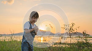 Little asian girl have happiness and enjoy in a green field with the background of the lake at sunset