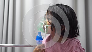 Little Asian girl having an oxygen mask and breathing through a nebulizer at the hospital. Concept of bronchitis, respiratory and