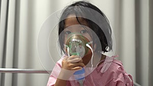 Little Asian girl having an oxygen mask and breathing through a nebulizer at the hospital. Concept of bronchitis, respiratory and