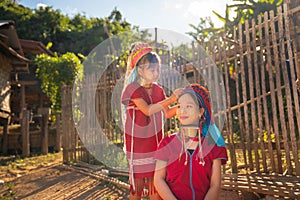 Little Asian girl help to set and decorate hair of her older sister and stay near road in Long Neck Karen Village in Thailand with