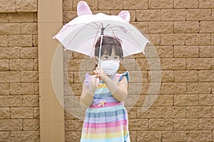 Little Asian girl holding an umbrella and wearing face mask protection from coronavirus illnesses