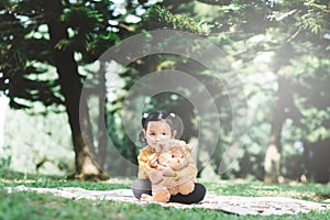 Little asian girl hugging her teddy bear in a park.