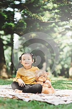 Little asian girl hugging her teddy bear in a park.