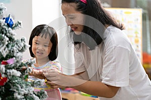 Little asian girl with mom decorating a Christmas tree together