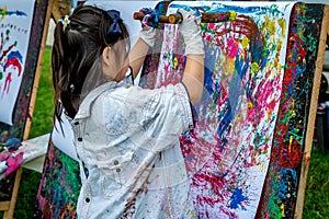 Little Asian girl painting on board with stick outdoors in park. Happy childhood and creativity