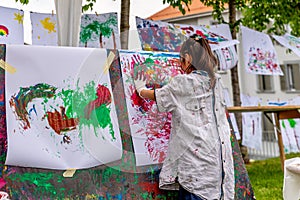 Little Asian girl painting on paper with hands outdoors. Happy childhood and creativity