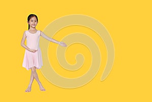 Little asian girl in pink leotard practise her ballet dance isolated on yellow background with copy space. Children is studying