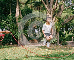 Little Asian girl playing with skipping rope jumping at green nature park.