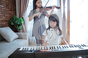 Little asian girl plays a musical instrument keyboard with her sister playing the violin together