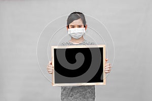 Little asian girl in a protective medical mask holding blackboard.