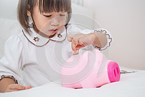 Little asian girl puting coin into piggy bank