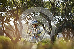 Little asian girl riding bike outdoors in city park