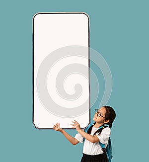 Little asian girl schooler holding huge smartphone, mockup