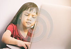 Little Asian girl is seriously working on a laptop computer.