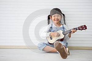 little asian girl sitting playing ukulele on white background with copy space