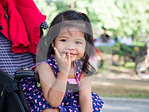 Little asian girl sitting in a stroller at public park. She have be smile and love in sign language.