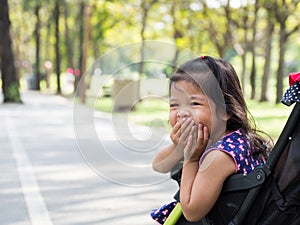 Little asian girl sitting in a stroller at public park. She look haply and laughing and gagging