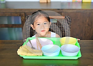 Little Asian girl waiting food at the table with many empty bowl