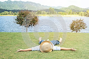 Little Asian girl wear weave hat and laying relax on green grass.