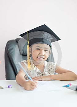 Little Asian girl wearing graduate hat doing homework and smile with happiness for success of education concept select focus