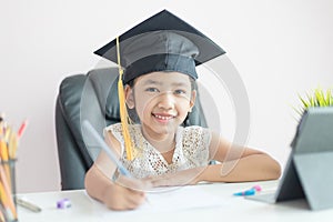 Little Asian girl wearing graduate hat doing homework and smile with happiness for success of education concept select focus